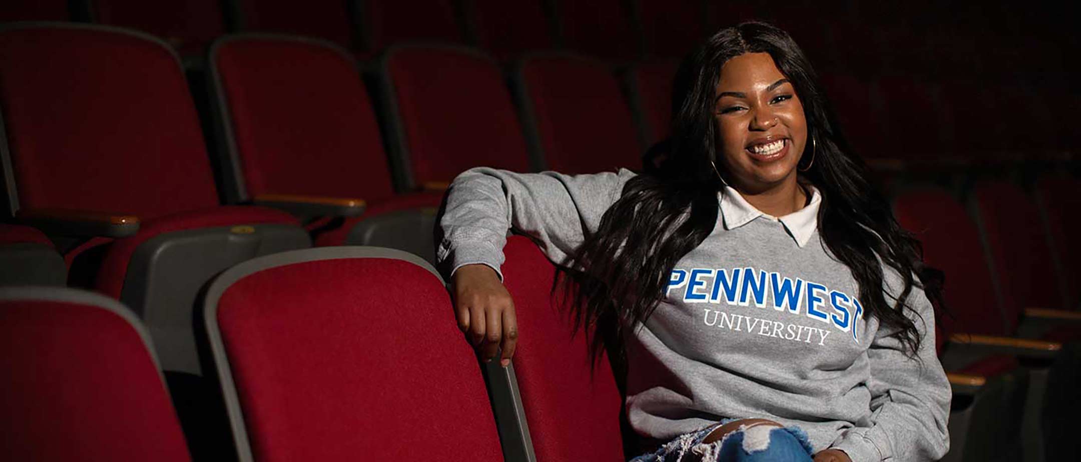 A theatre student sits in the audience seating and poses for the camera.