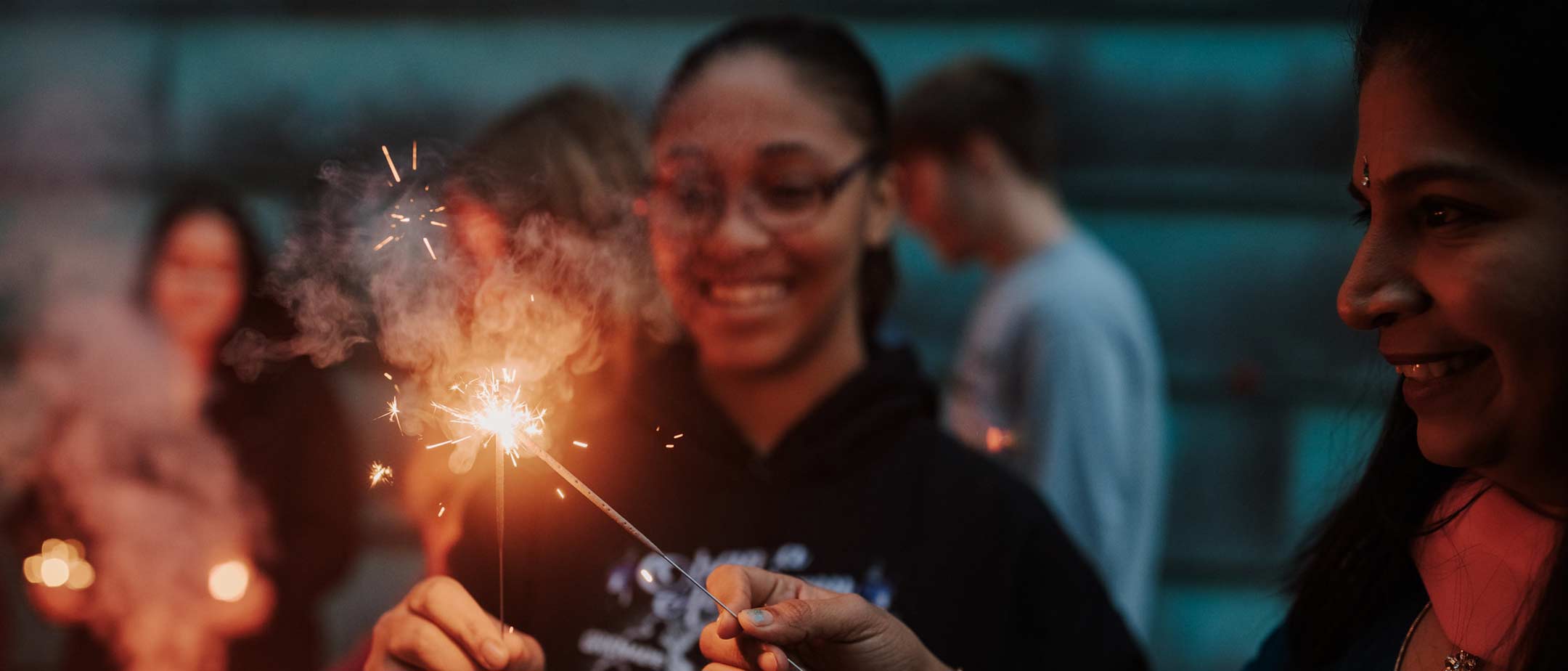 Diverse students using sparklers on campus and smiling.